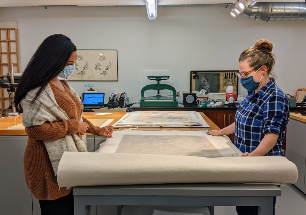 Two women observe a large work of art on a paper scroll