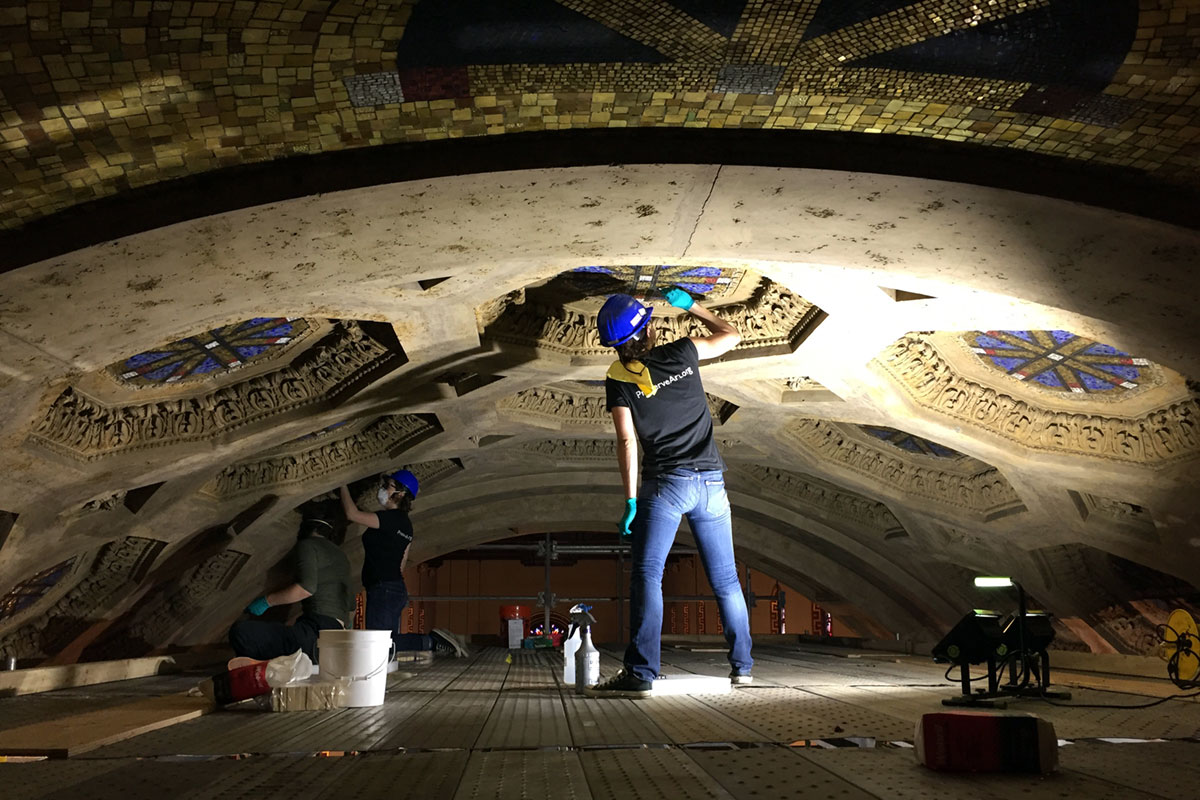 MACC practitioners work on scaffolding to restore a mural on a ceiling